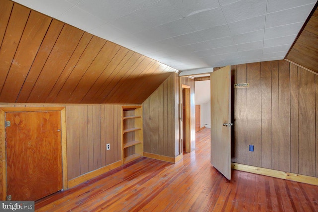 bonus room with wood-type flooring, lofted ceiling, a baseboard heating unit, and wooden walls