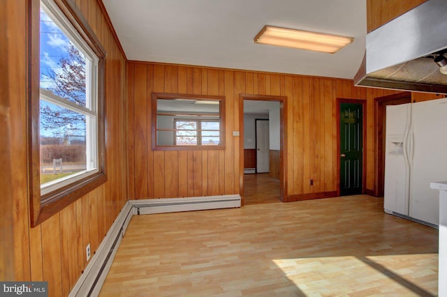 unfurnished room featuring light wood-type flooring, a baseboard radiator, and wood walls