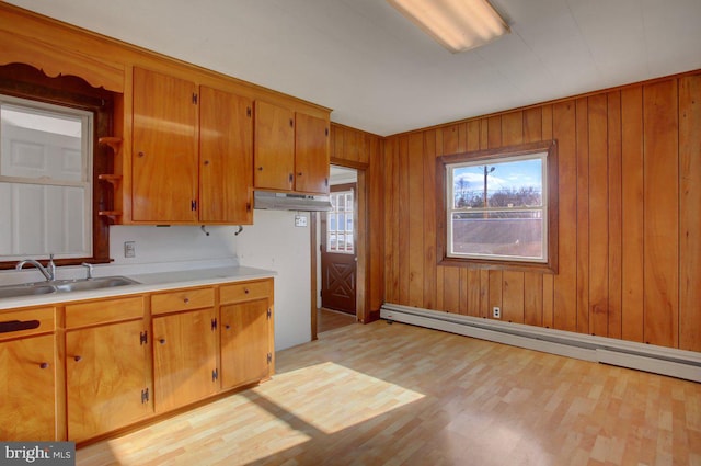 kitchen with wood walls, a baseboard heating unit, sink, and light wood-type flooring