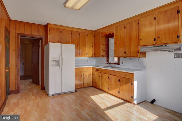 kitchen featuring light hardwood / wood-style floors, wooden walls, white refrigerator with ice dispenser, and sink