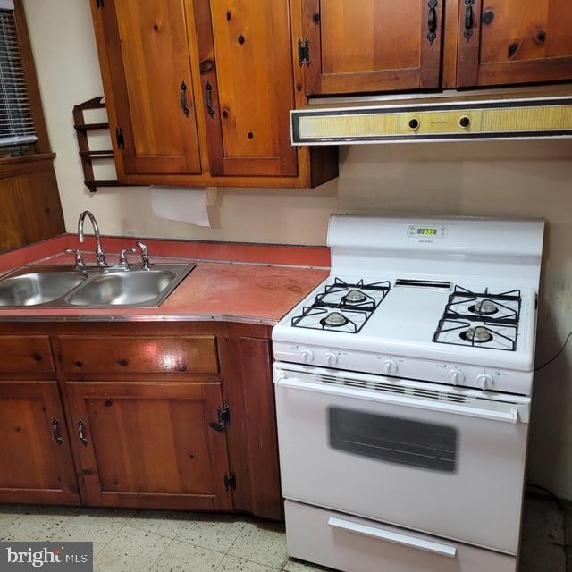 kitchen featuring white range with gas cooktop, range hood, and sink