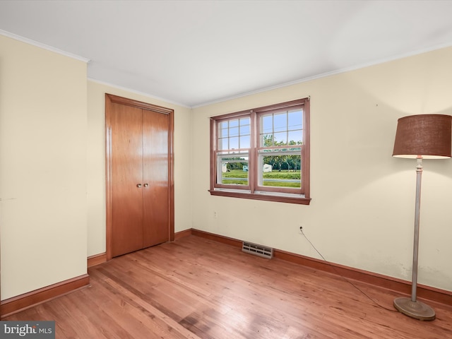 unfurnished bedroom featuring crown molding, light hardwood / wood-style floors, and a closet