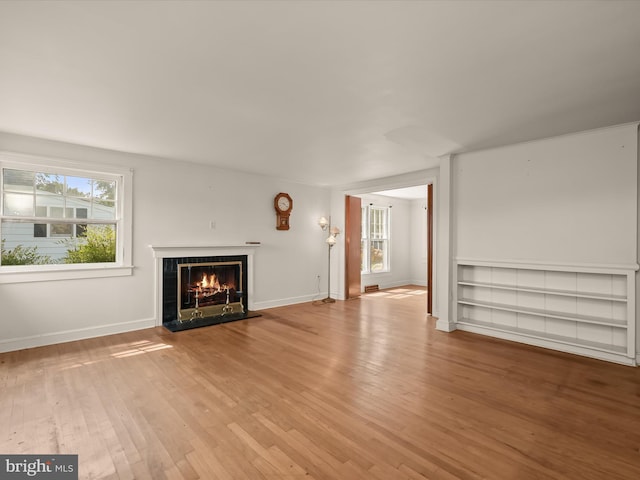 unfurnished living room featuring a tiled fireplace, a wealth of natural light, and light wood-type flooring