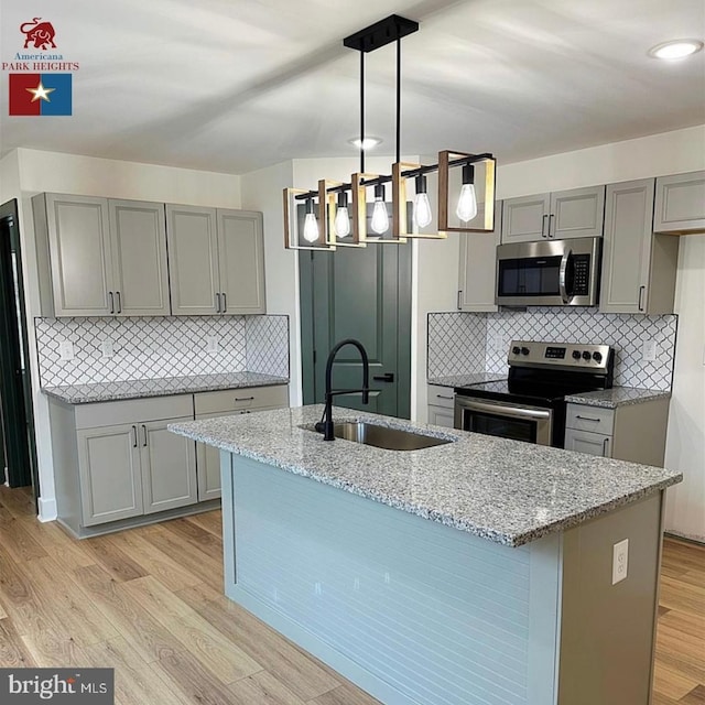 kitchen with appliances with stainless steel finishes, sink, pendant lighting, and light stone counters