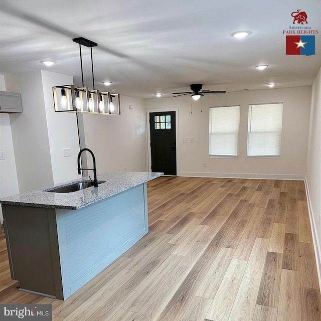 kitchen featuring sink, gray cabinets, hanging light fixtures, light stone counters, and light hardwood / wood-style floors