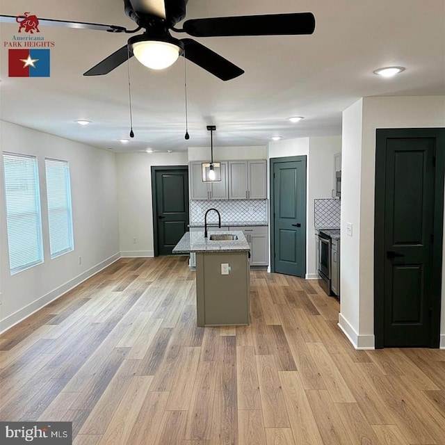 kitchen with sink, light hardwood / wood-style flooring, gray cabinets, pendant lighting, and a kitchen island with sink