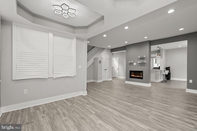 unfurnished living room featuring a tray ceiling and light hardwood / wood-style floors