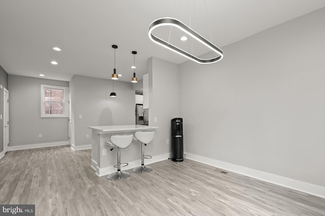 kitchen with light hardwood / wood-style flooring, a breakfast bar, hanging light fixtures, stainless steel refrigerator with ice dispenser, and white cabinets