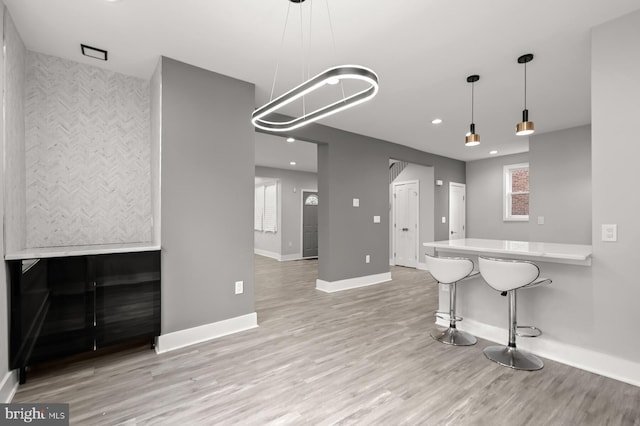 kitchen with decorative light fixtures, a kitchen breakfast bar, kitchen peninsula, and light hardwood / wood-style flooring