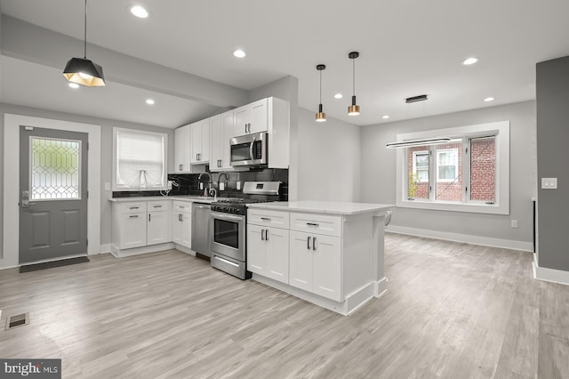 kitchen featuring appliances with stainless steel finishes, decorative light fixtures, white cabinets, light hardwood / wood-style floors, and kitchen peninsula