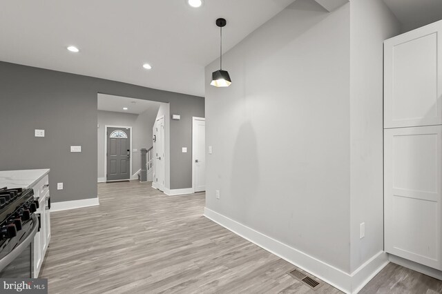 kitchen with gas range, decorative light fixtures, light stone countertops, light hardwood / wood-style floors, and white cabinets