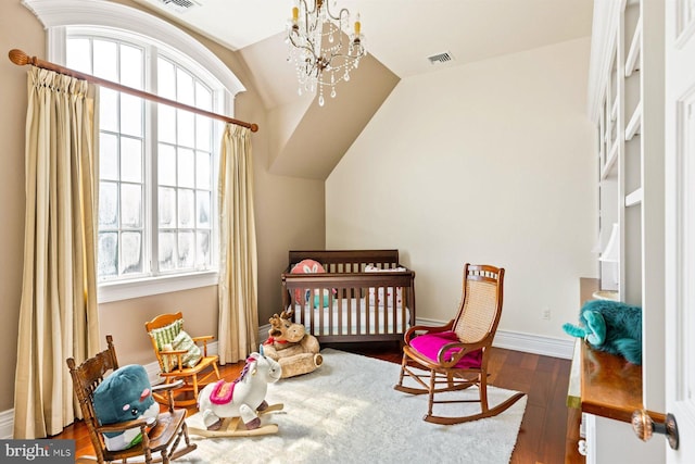 interior space featuring hardwood / wood-style floors, an inviting chandelier, vaulted ceiling, and a crib