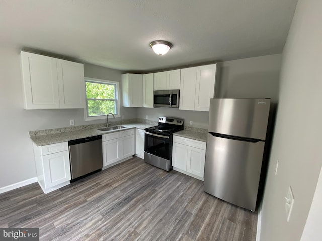 kitchen with sink, light stone counters, appliances with stainless steel finishes, hardwood / wood-style floors, and white cabinets