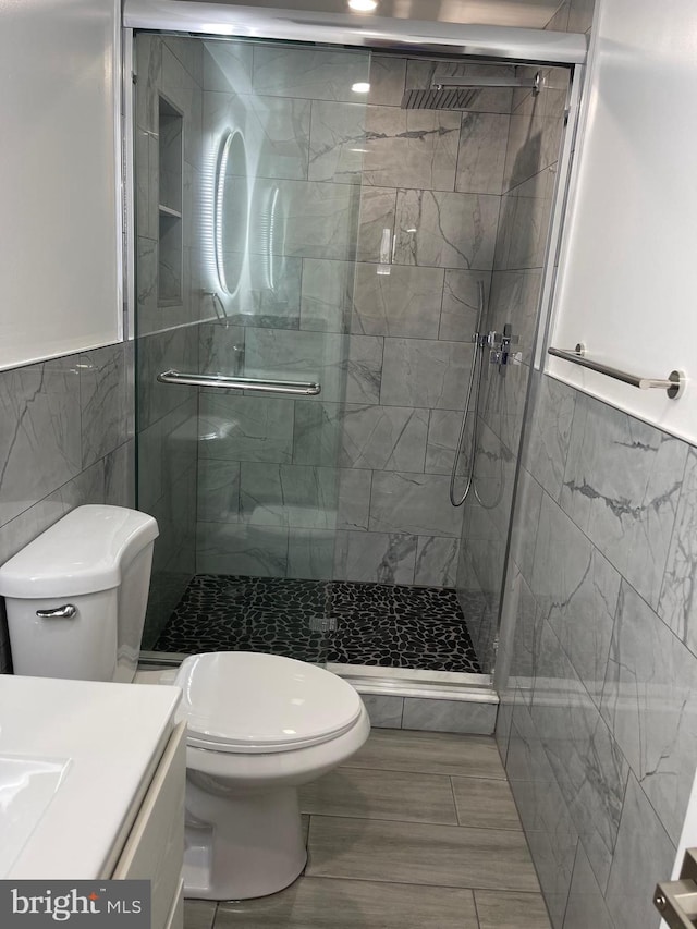 bathroom featuring tile walls, vanity, a shower with door, and toilet