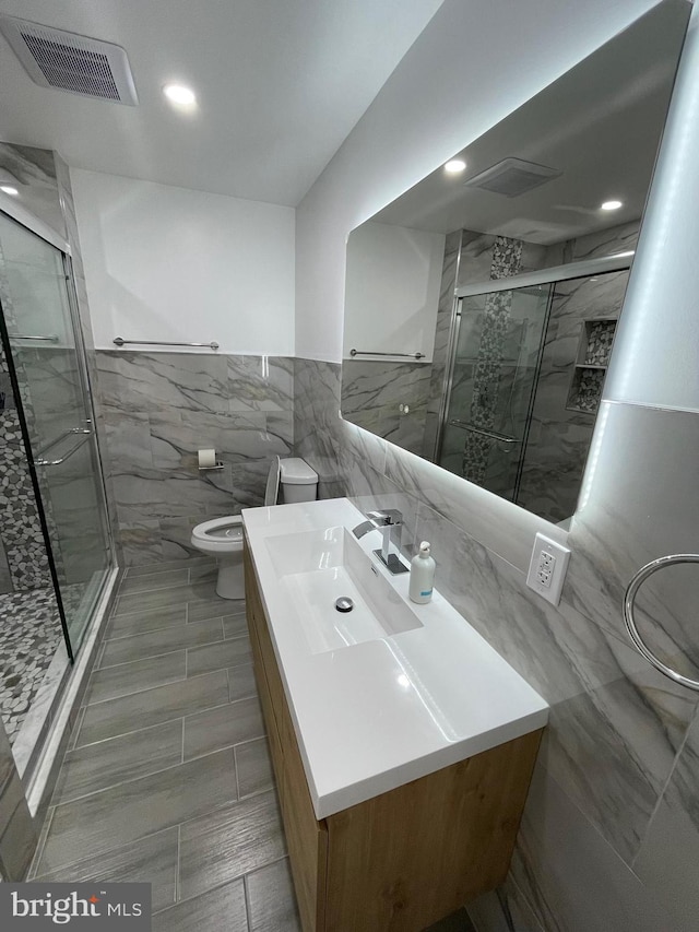 bathroom featuring vanity, toilet, a shower with door, and tile walls