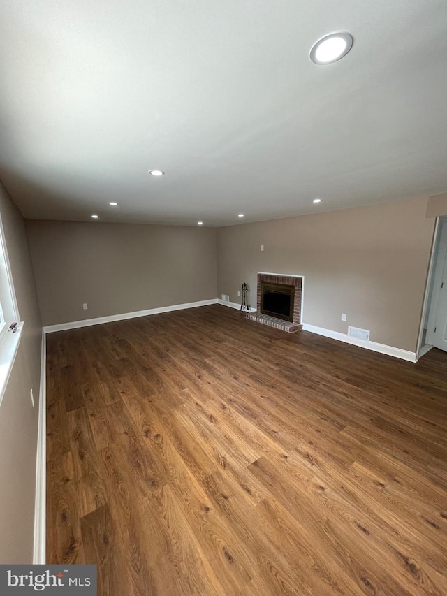 unfurnished living room with wood-type flooring and a brick fireplace