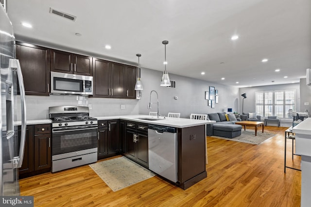 kitchen featuring kitchen peninsula, hanging light fixtures, sink, light wood-type flooring, and appliances with stainless steel finishes