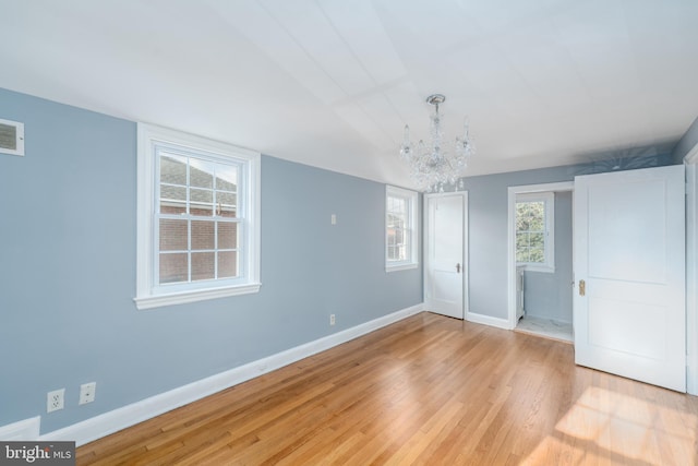 unfurnished bedroom featuring an inviting chandelier and light hardwood / wood-style flooring