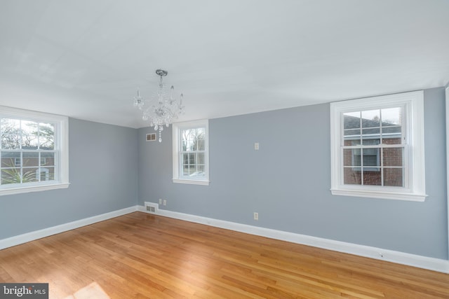 empty room with plenty of natural light, a chandelier, and light wood-type flooring