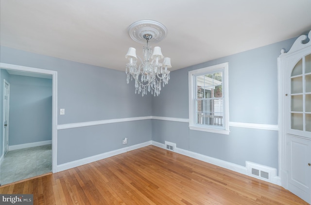 spare room with an inviting chandelier and hardwood / wood-style flooring