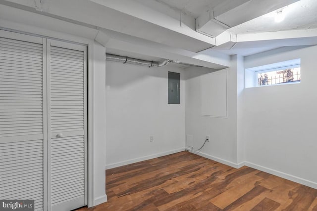 basement featuring dark wood-type flooring, electric panel, and baseboards