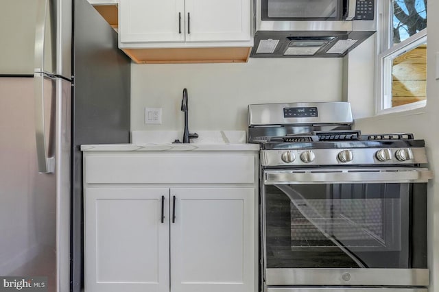 kitchen with stainless steel appliances, white cabinetry, a sink, and light stone countertops