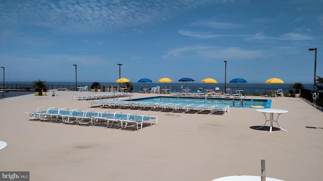 community pool with a patio, a water view, and fence