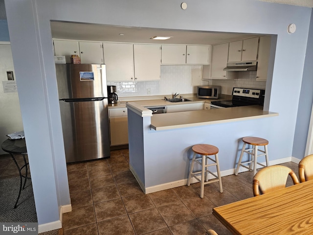 kitchen featuring appliances with stainless steel finishes, a sink, under cabinet range hood, and a peninsula