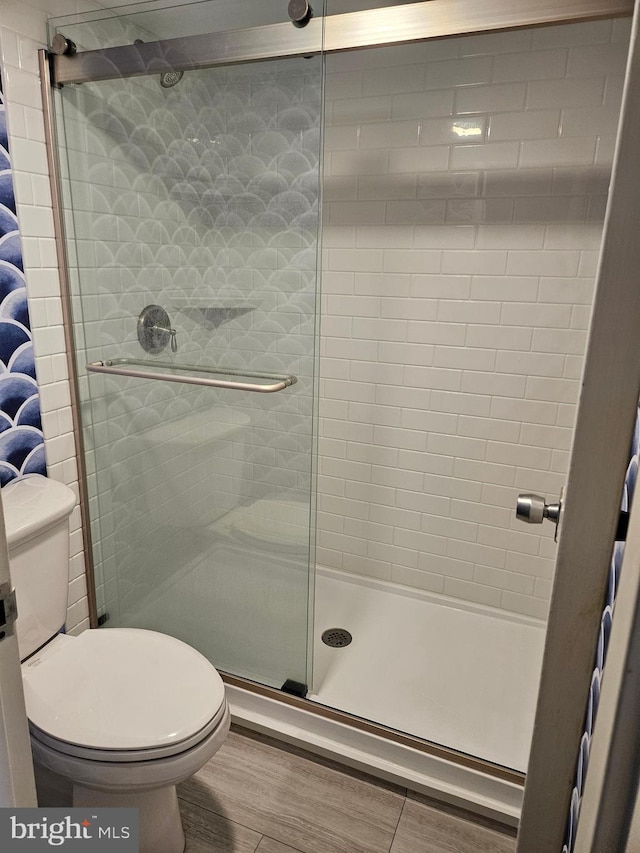 full bath featuring a stall shower, wood finished floors, and toilet