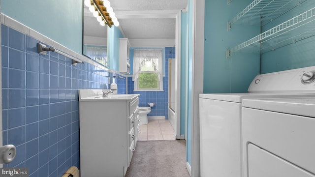 clothes washing area with tile walls, a textured ceiling, independent washer and dryer, and light tile patterned floors