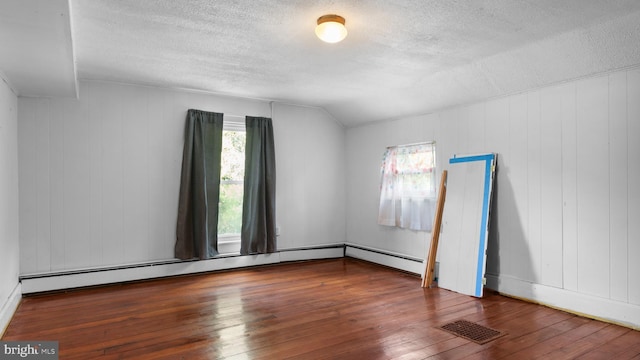 empty room featuring dark wood-type flooring, vaulted ceiling, a textured ceiling, and a baseboard heating unit