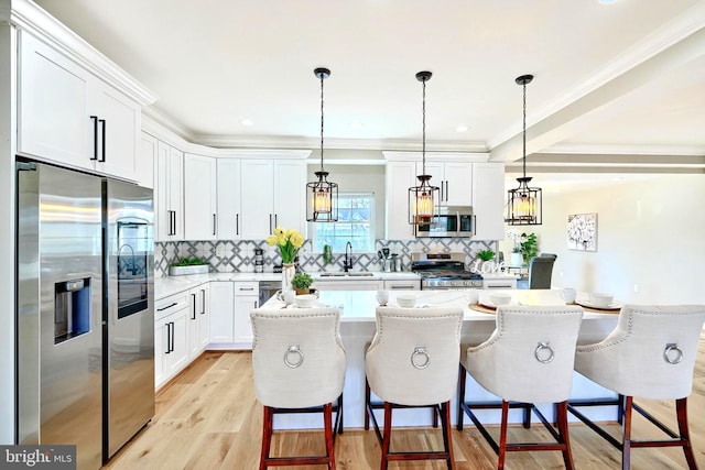 kitchen with pendant lighting, appliances with stainless steel finishes, white cabinetry, a kitchen breakfast bar, and a kitchen island