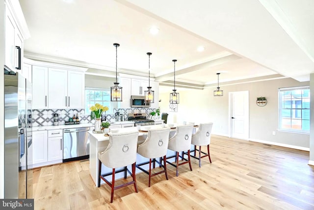 kitchen with appliances with stainless steel finishes, white cabinetry, a breakfast bar area, hanging light fixtures, and a center island