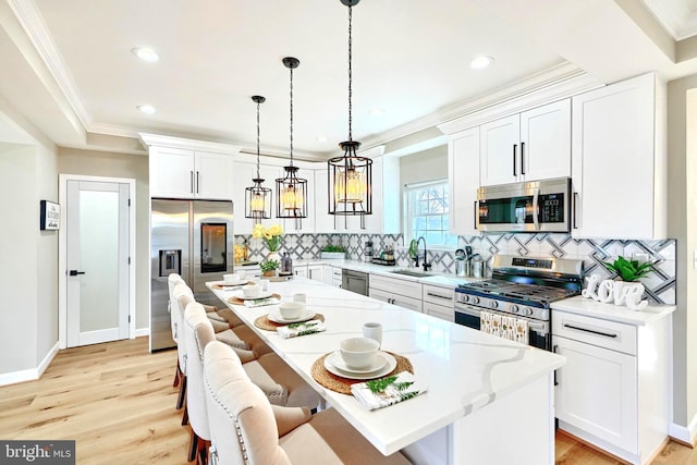 kitchen featuring a breakfast bar area, appliances with stainless steel finishes, hanging light fixtures, white cabinets, and a kitchen island