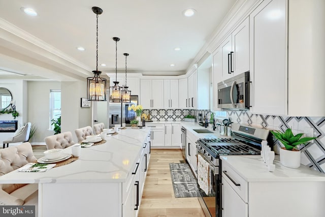 kitchen with pendant lighting, appliances with stainless steel finishes, white cabinetry, light stone counters, and a kitchen island