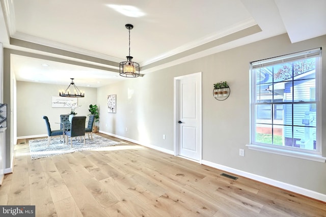 unfurnished dining area featuring ornamental molding, a raised ceiling, a chandelier, and light wood-type flooring