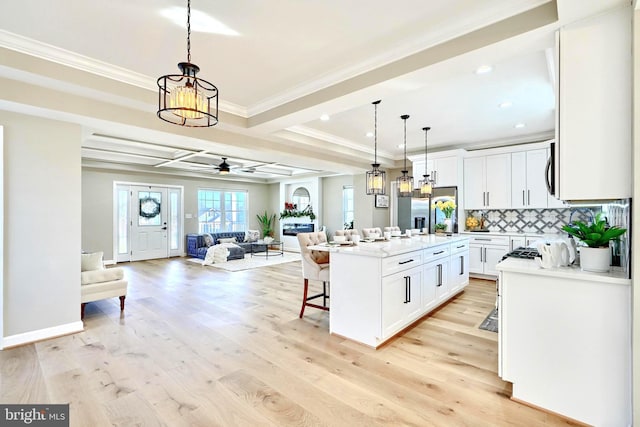 kitchen with decorative light fixtures, white cabinetry, backsplash, a kitchen island with sink, and light hardwood / wood-style flooring