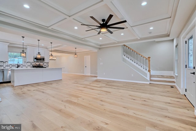 unfurnished living room featuring ceiling fan, sink, coffered ceiling, crown molding, and light wood-type flooring