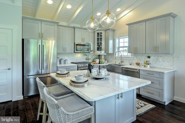 kitchen with appliances with stainless steel finishes, hanging light fixtures, a center island, light stone counters, and lofted ceiling with beams