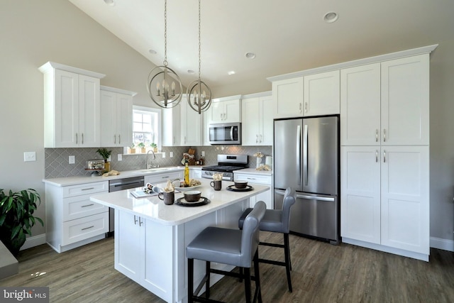 kitchen with appliances with stainless steel finishes, white cabinets, vaulted ceiling, a kitchen island, and dark hardwood / wood-style flooring