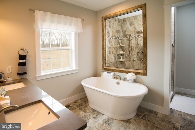 full bathroom featuring a sink, baseboards, double vanity, a soaking tub, and stone finish flooring