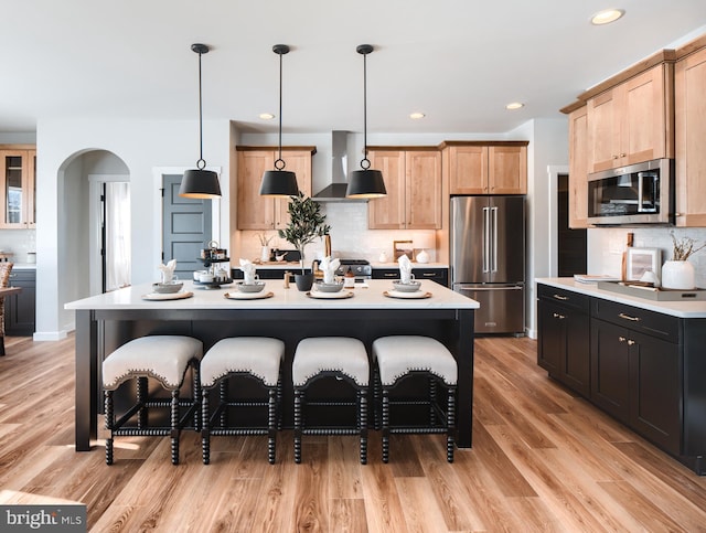 kitchen with hanging light fixtures, stainless steel appliances, light countertops, and an island with sink