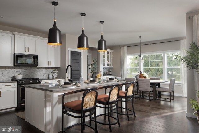 kitchen with a kitchen island with sink, white cabinetry, high end range, dark countertops, and glass insert cabinets