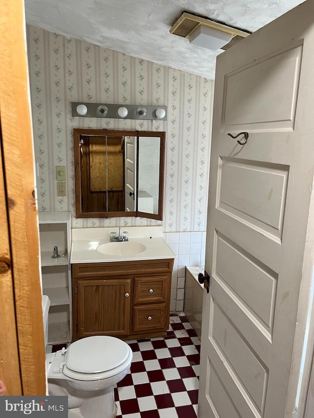 bathroom with toilet, tile walls, a washtub, vanity, and a textured ceiling