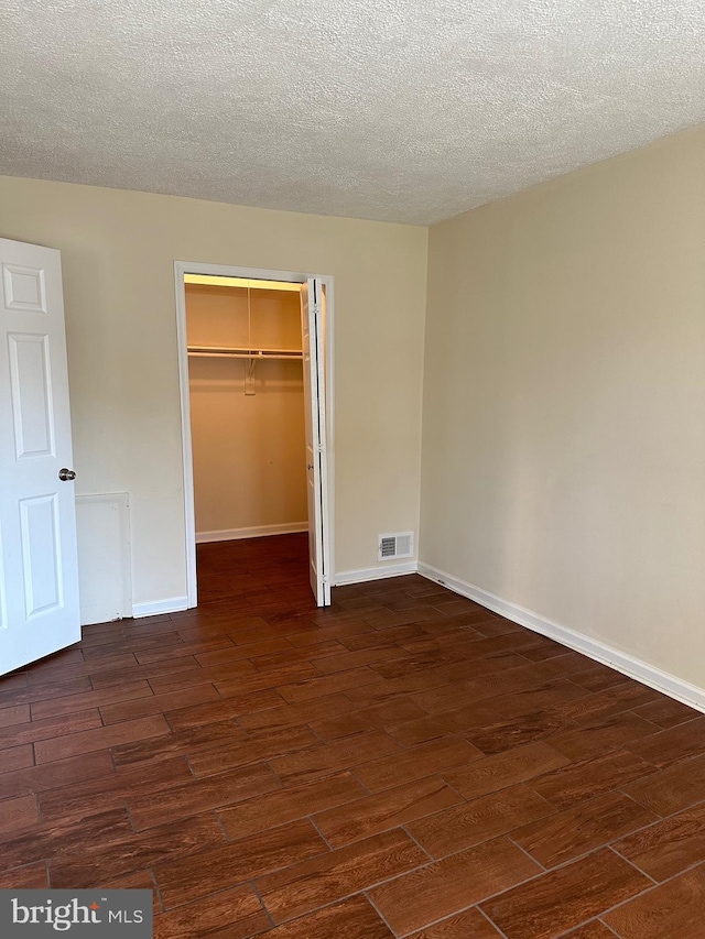 unfurnished bedroom featuring a spacious closet, a textured ceiling, dark hardwood / wood-style flooring, and a closet