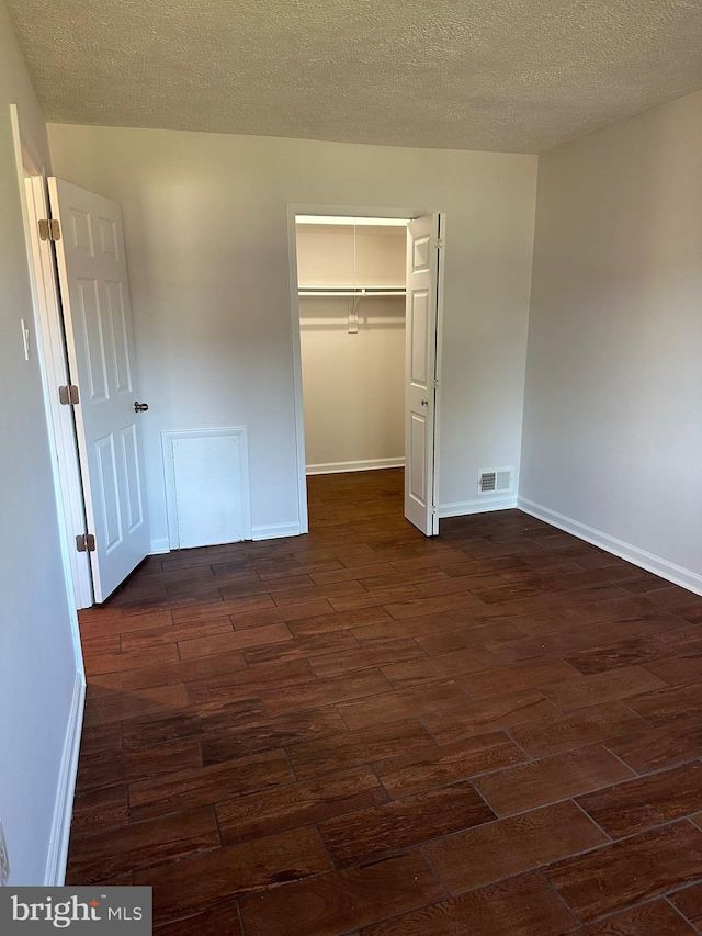 unfurnished bedroom with dark wood-type flooring, a spacious closet, a closet, and a textured ceiling