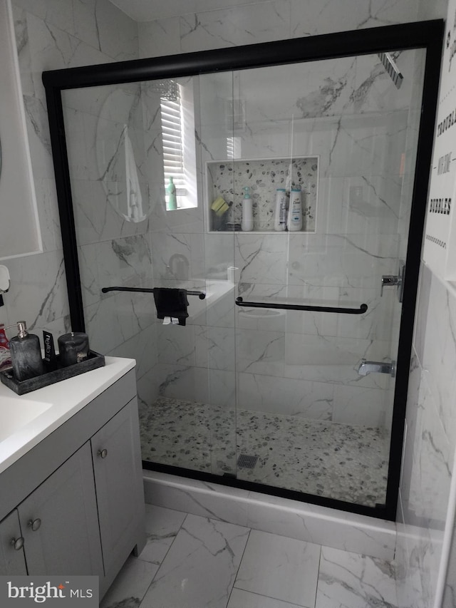 bathroom with tile patterned floors, vanity, a shower with door, and tile walls