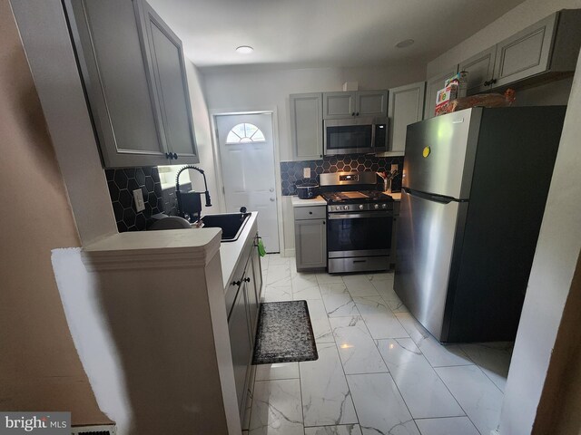 kitchen featuring stainless steel appliances, backsplash, sink, and gray cabinetry