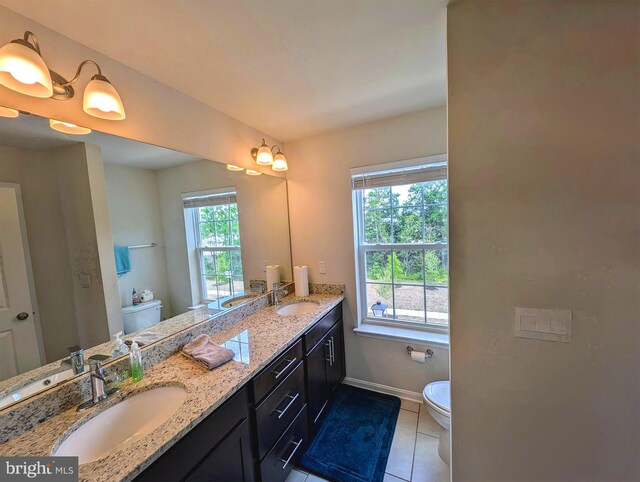 bathroom featuring toilet, a wealth of natural light, tile patterned flooring, and double sink vanity