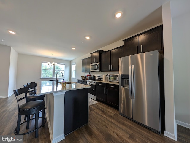 kitchen with sink, stainless steel appliances, light stone counters, an island with sink, and decorative light fixtures